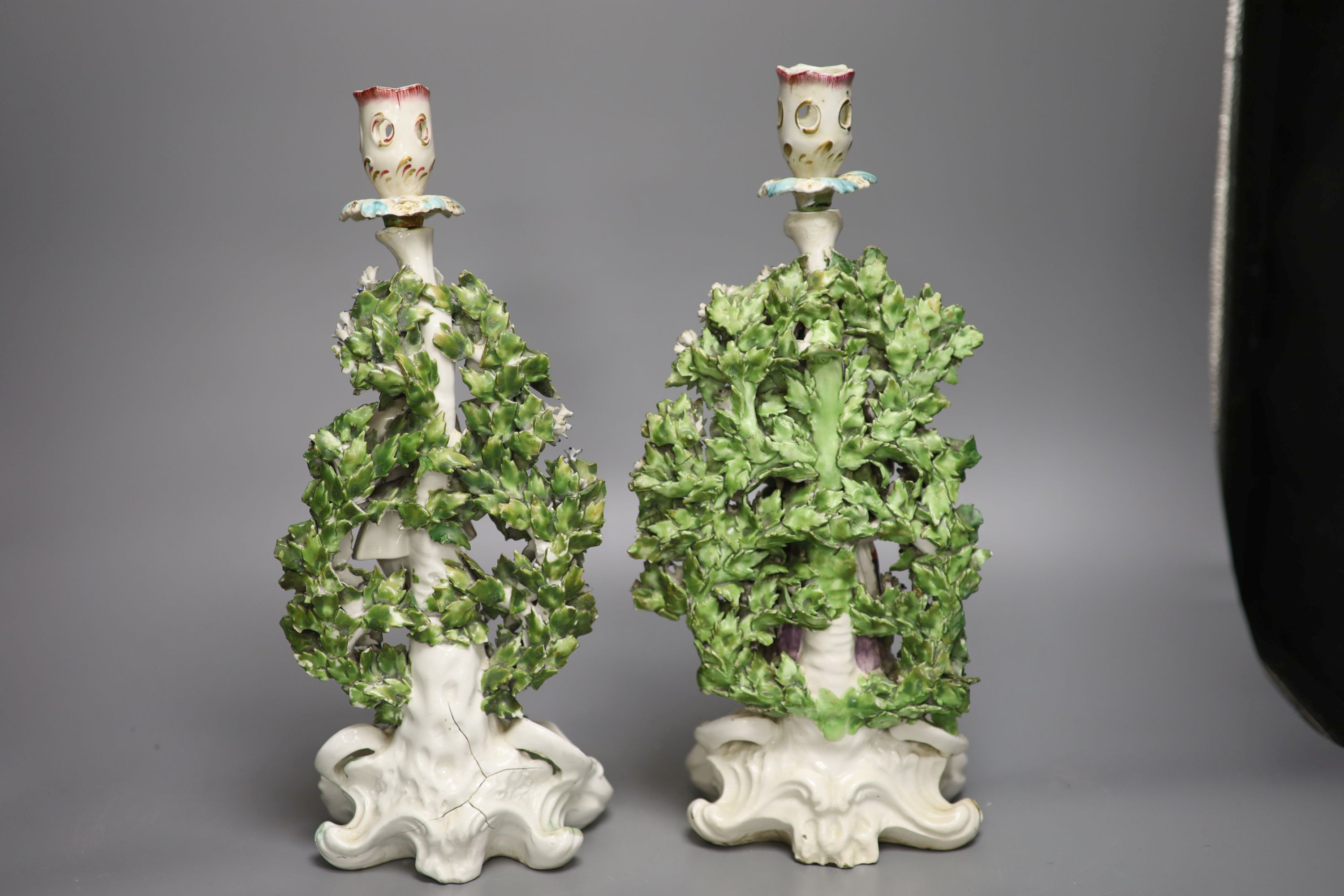 A pair of Derby candlestick figures of the Italian Farmer and wife, he holding a rooster, and her a chicken standing on a rococo scroll